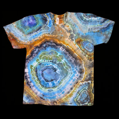 Front of a tie-dyed t-shirt with large concentric geode rings in blue, orange, gray, and green on a black background.