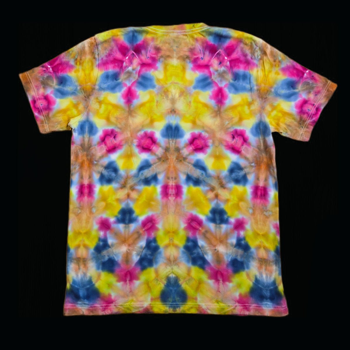 Back of the same t-shirt showing the mirrored fold tie-dye repeat in magenta, yellow, blue, and orange with symmetry along the center spine.